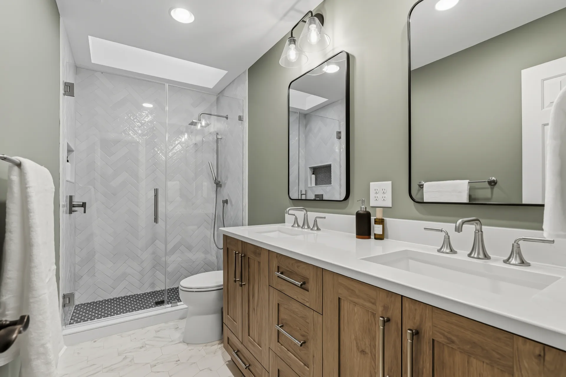 Bathroom remodel with glass walk-in shower, sage green walls, and wood double vanity