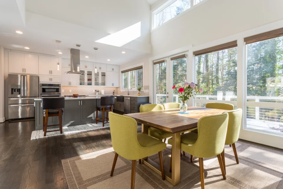 Open kitchen and dining area with white cabinetry, gas range, vaulted ceiling with skylights, and chartreuse velvet dining chairs