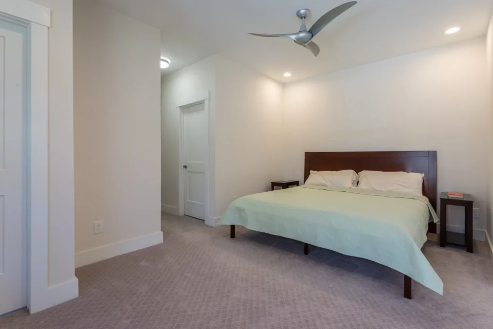 Bright primary bedroom with a king bed, mint green coverlet, modern silver ceiling fan, and plush carpet