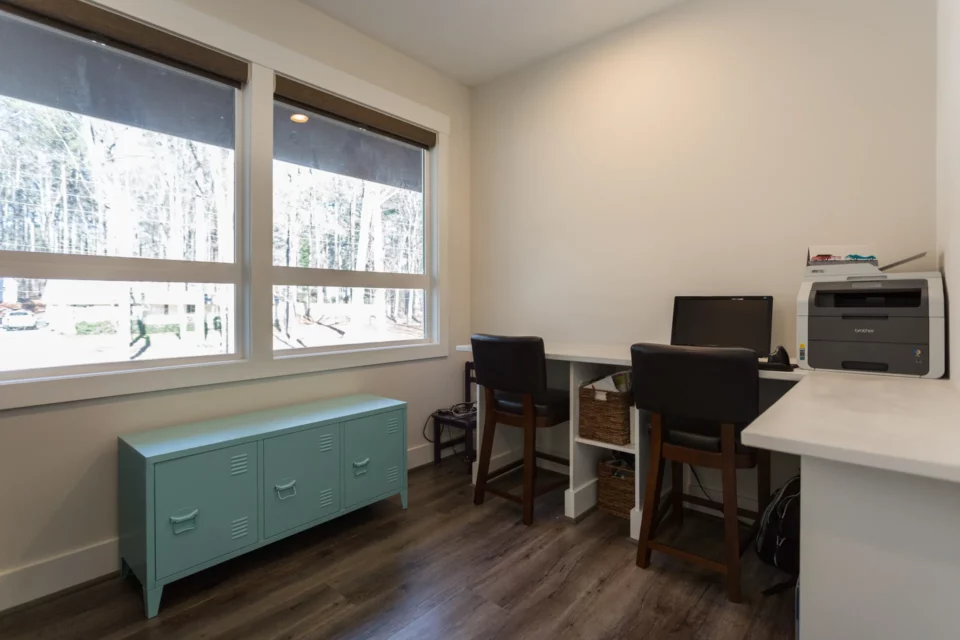 Home office with built-in desk, leather counter stools, bay window, and a mint green storage console