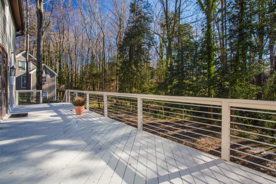Large rear deck with light-stained boards and cable railings overlooking the wooded backyard