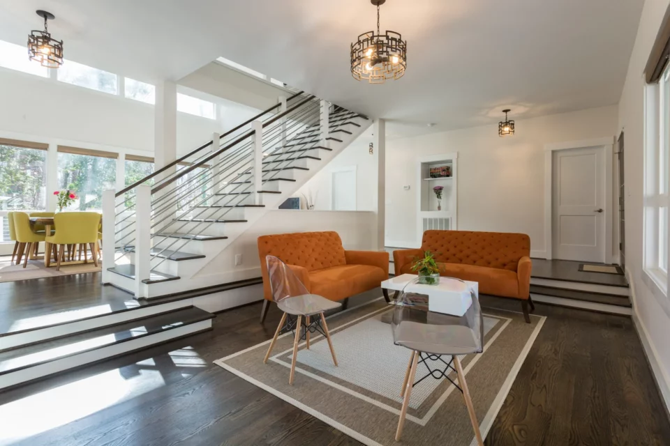 Open foyer and living room with two burnt orange velvet chairs facing modern floating stairs