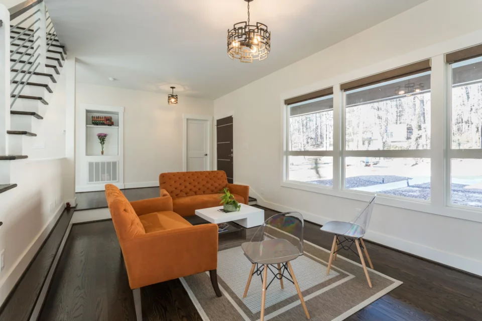 Bright living room with orange velvet seating, large picture windows, and a geometric pendant light