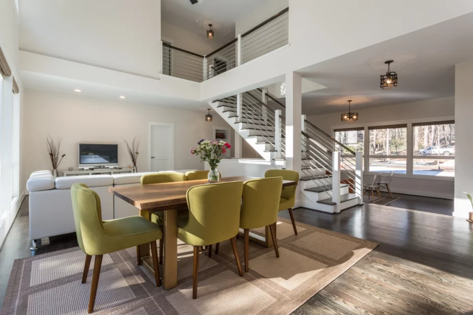 Open dining area with chartreuse velvet chairs around a wood table, looking back toward the floating staircase and upstairs walkway