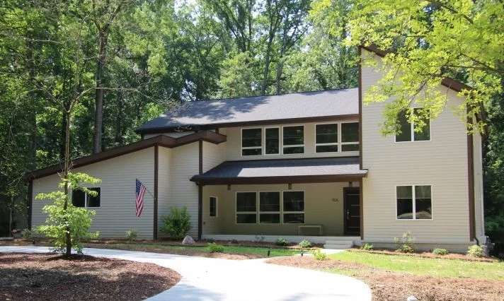 Completed two-story home with cream siding, brown trim, asymmetric rooflines, and a front porch with American flag