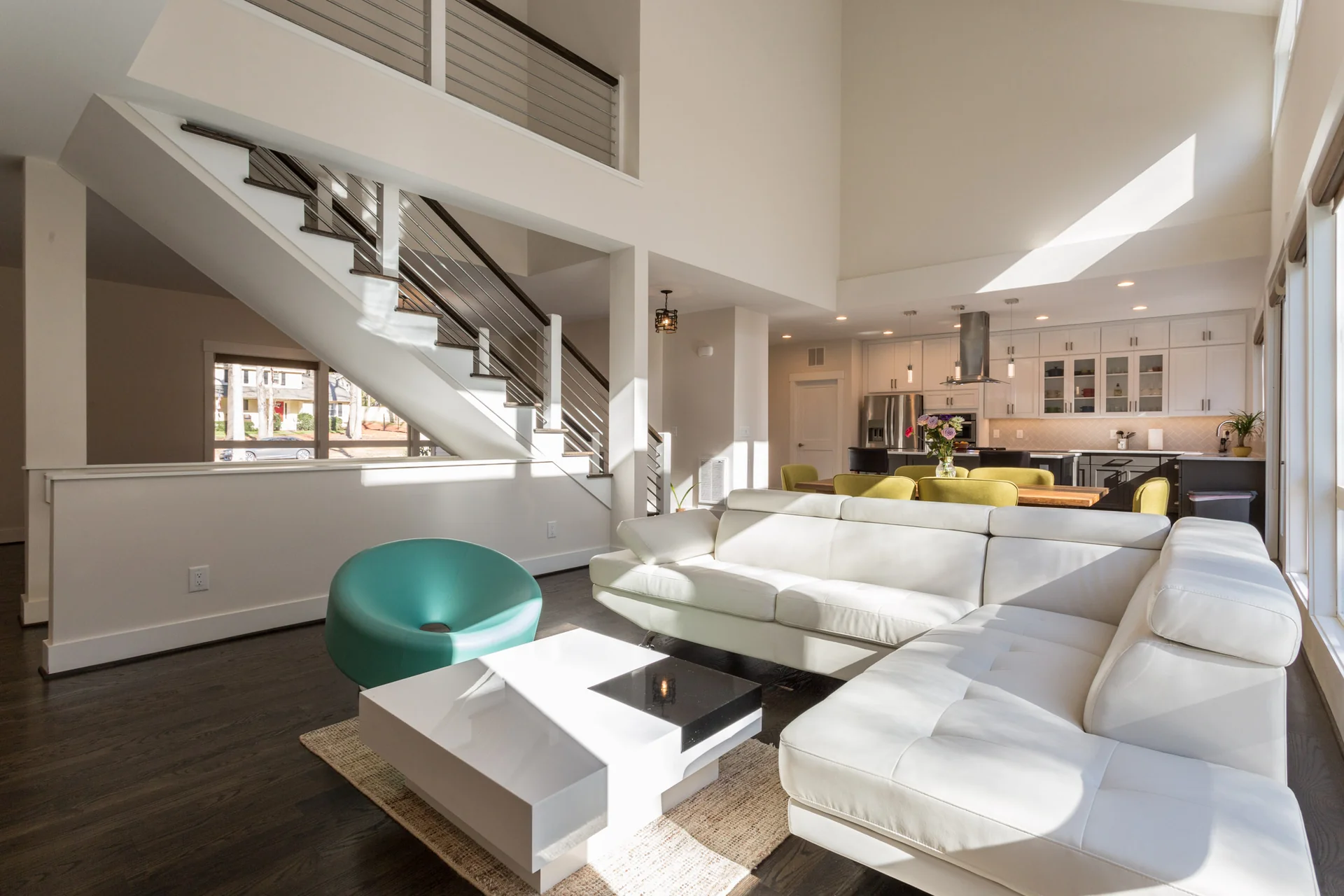 Modern open-concept living room with white sectional, mid-century coffee table, and floating stairs with cable railings under a vaulted ceiling