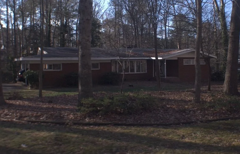 Original single-story red brick ranch home set back in the wooded lot before the remodel