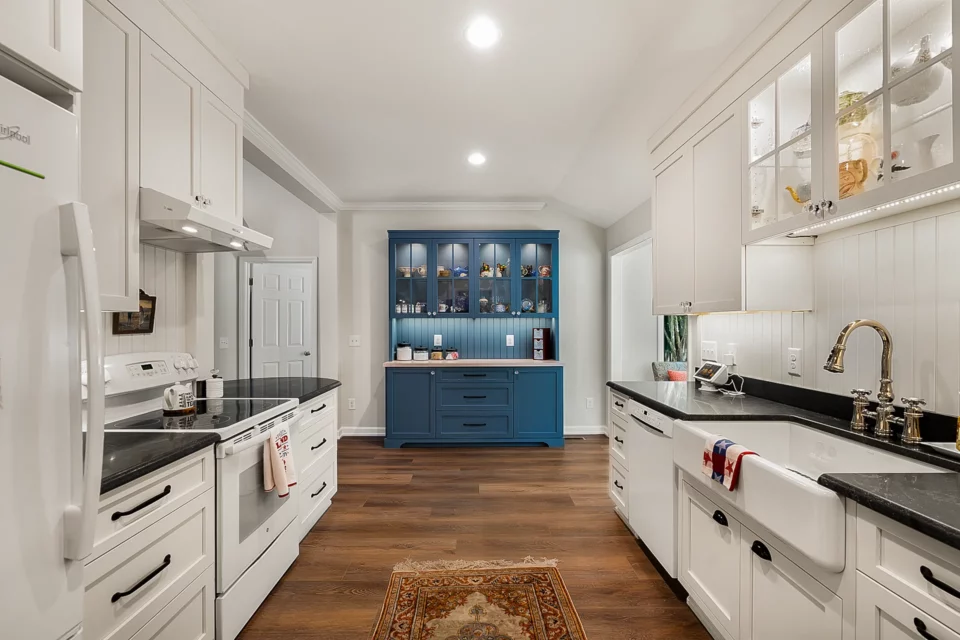 White shaker galley kitchen with farmhouse sink and built-in blue china cabinet at the end